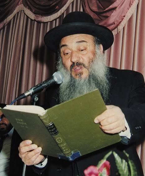 Rabbi Nissim Yagen reading from an open book beside a microphone