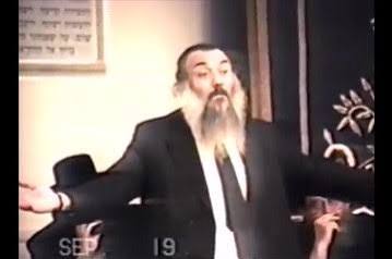 Archival still of Rabbi Nissim Yagen speaking with his arms extended